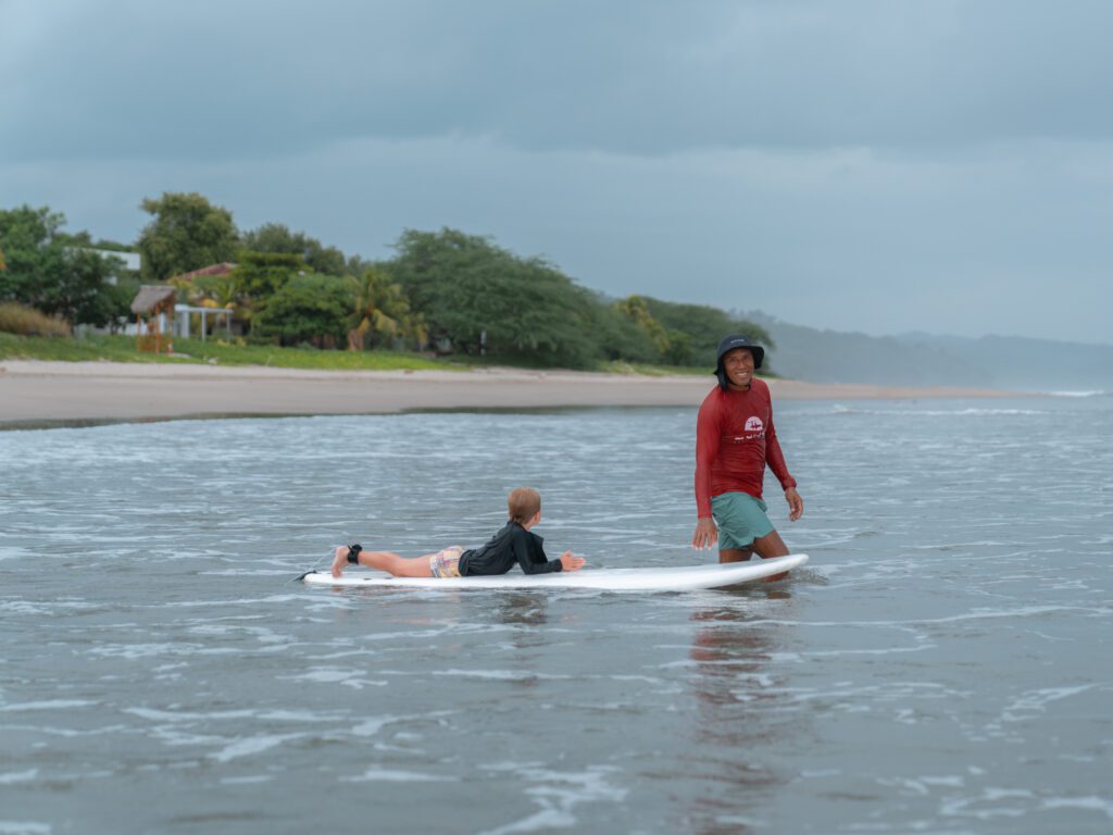 boy surfing with a surf instructor on Playa Los Perros at Rancho Santana